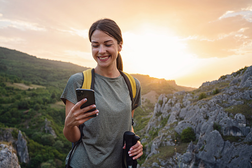 Solo female hiker, using her mobile phone during her hike, to send some text messages or to see her location on GPS app, while enjoying her solo mountain adventure