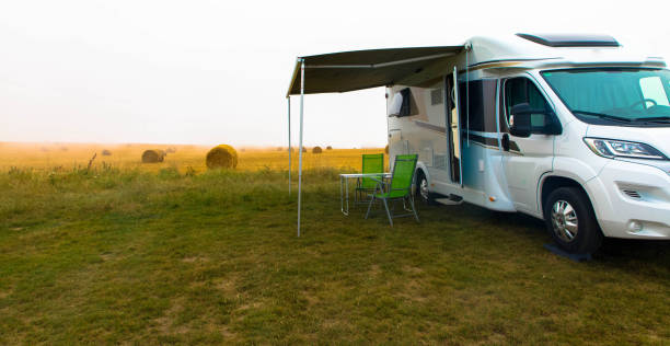 Mobile home ist standing on green lawn. Empty folding chairs and table under canopy near new modern recreational vehicle trailer trailer. Tourism and vacations concept. stock photo