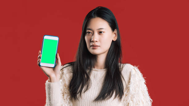 Mobile phone with copyspace template. Female portrait asian woman at the studio with smartphone on red background. Concept with real people and empty white screen of device for application  smart phone green background stock pictures, royalty-free photos & images
