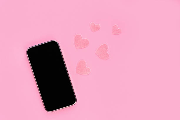Mock up phone with black screen with felt heart on pink background. Copy space. Online conversation, birthday or Valentine's Day stock photo