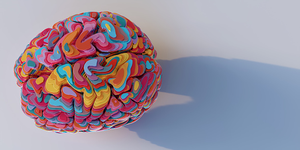 a model of a brain viewed from above, sliced into many horizontal multi-coloured layers of shiny metallic material, stacked up to form brain model. The model sits on a plain white surface with shadow.