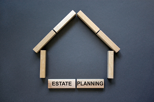 Model of a wooden house from wooden blocks. Words 'estate planning'. Copy space. Business concept. Beautiful grey background.