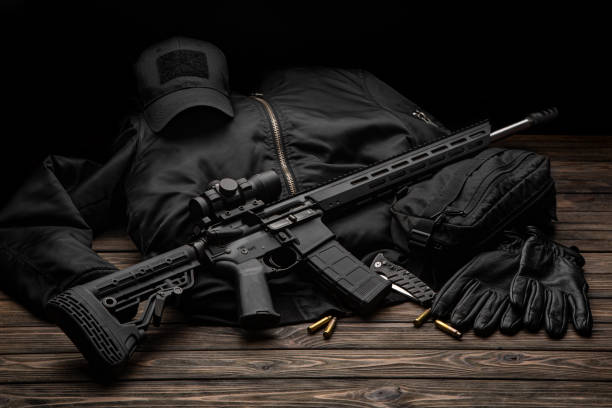 Modern automatic rifle with a telescopic sight on a dark background. Jacket, cap, gloves on a wooden table. The uniform of a guard or a mercenary. stock photo