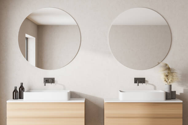 Modern bathroom with white walls, two sink with round mirrors and left window light. stock photo