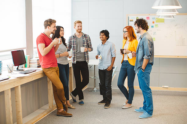 Modern business. Group of young creative people collaborating in an office. having coffee break, standing together and holding cups with coffee. coffee break stock pictures, royalty-free photos & images