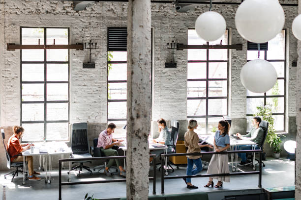 Modern Companies:  Group of Young Business People at a Spacious Loft Open Space Coworking Office Working Together Large group of freelance creative professionals working together. busy office stock pictures, royalty-free photos & images