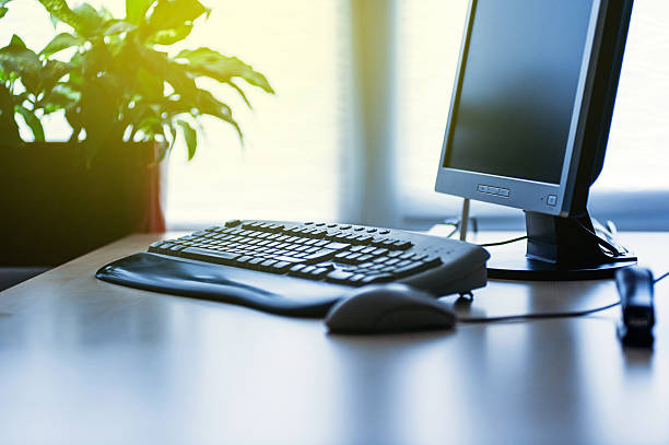 Modern Computer on desk in office lit by sun Personal computer on a desk in bright modern office lit by yellow sun coming from the window computer training stock pictures, royalty-free photos & images
