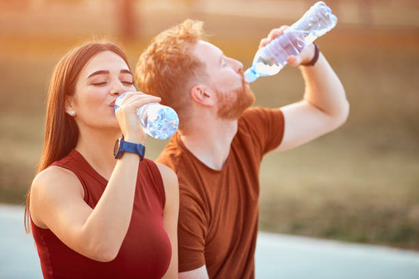 coppia moderna che fa una pausa in un parco urbano durante il jogging / esercizio fisico. - bere acqua foto e immagini stock