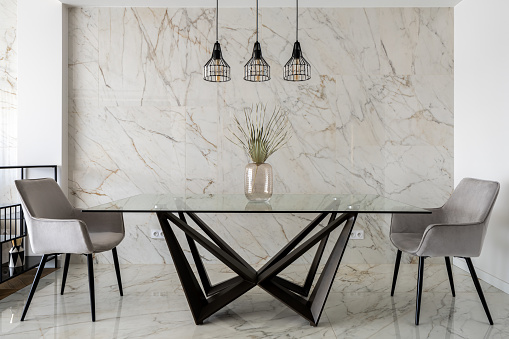 Stylish dining room with marble tiles on wall and floor and big, modern glass table with two chairs