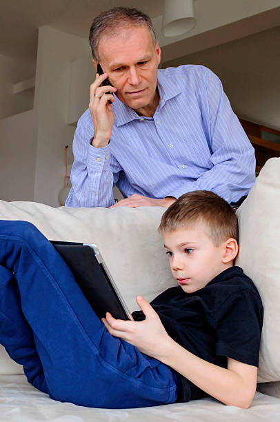 Modern father and son with electronics on sofa stock photo