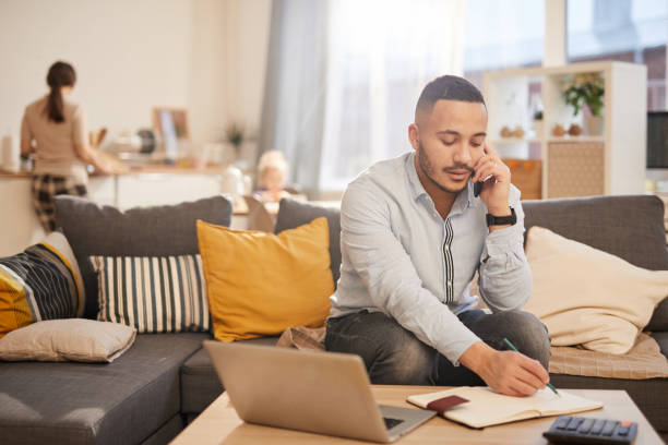 Modern Father Working from Home Portrait of modern mixed race man speaking by phone while working from home in cozy interior, copy space working at home stock pictures, royalty-free photos & images