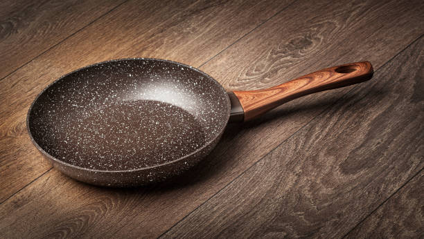 Modern frying pan with non-stick granite coating Modern frying pan with non-stick granite coating isolated on a wooden surface background. granitic stock pictures, royalty-free photos & images