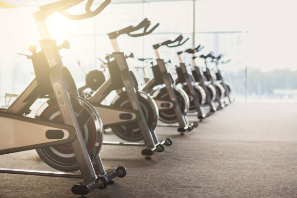 Modern gym interior with equipment, fitness exercise bikes Modern gym interior with equipment. Fitness club with row of training exercise bikes. Healthy lifestyle concept peloton stock pictures, royalty-free photos & images