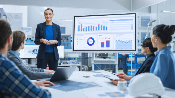 modern industrial factory meeting: confident female engineer uses interactive whiteboard, makes report to a group of engineers, managers talks and shows statistics, growth and analysis information - big data imagens e fotografias de stock