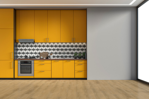 Empty modern kitchen with saffron yellow/ orange high wooden kitchen cabinets with tiled pattern background,  ceiling led lights. A large light gray plaster wall background on hardwood floor with copy space and windows on a side. Retro style of 70's. 3D rendered image.