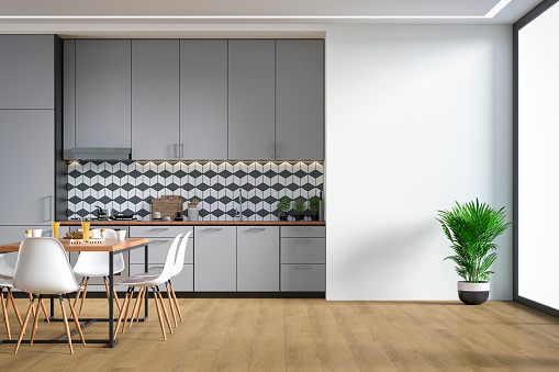 Empty modern kitchen with light gray high wooden kitchen cabinets with tiled pattern background,  ceiling led lights, dining table and  chairs. A potted plant in front of a large white plaster wall background on hardwood floor with copy space and windows on a side. 3D rendered image.