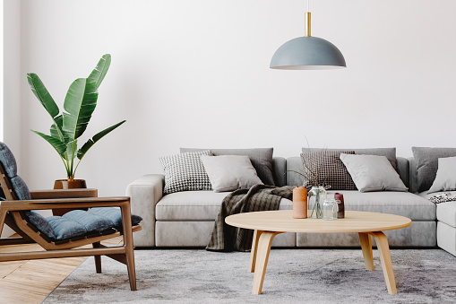 Modern living room setup with classic parquet floor. Furnished with light gray sofa, blue arm chair with wooden frame, modern blue ceiling lamp, wooden coffee table and gray carpet.