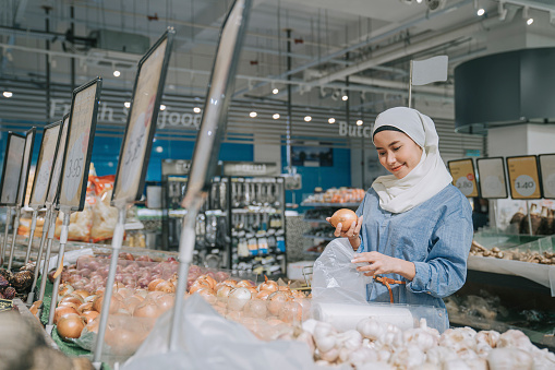 modern malay woman with hijab and modest clothing shopping buying onions in supermarket during weekend