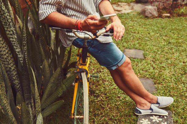 Modern man using cellphone while sitting on the grass with old bicycle. stock photo