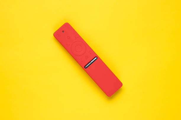Modern TV remote in silicone case on a yellow background. Top view, minimalism stock photo