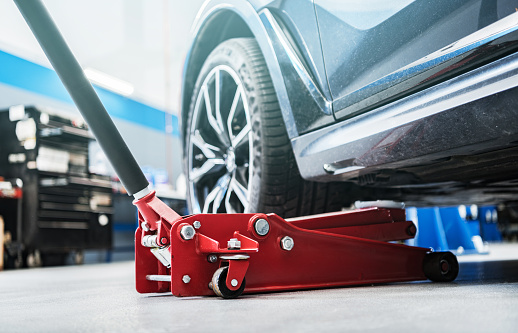 Modern Vehicle and the Floor Jack Lift Vehicle Servicing and Maintenance Inside Auto Service Center.