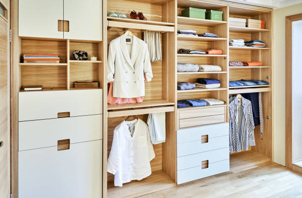 Modern wardrobe with clothes hanging on slide out racks and folded on the shelves. Modern furniture Internal details of the wooden wardrobe with slide out rack for coathangers. Modern wardrobe with clothes hanging on slide out racks and folded on the shelves. Modern furniture closet stock pictures, royalty-free photos & images