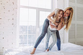 Attractive young woman and her little cute daughter are having fun in bed while being at home together. Happy Mother's Day!