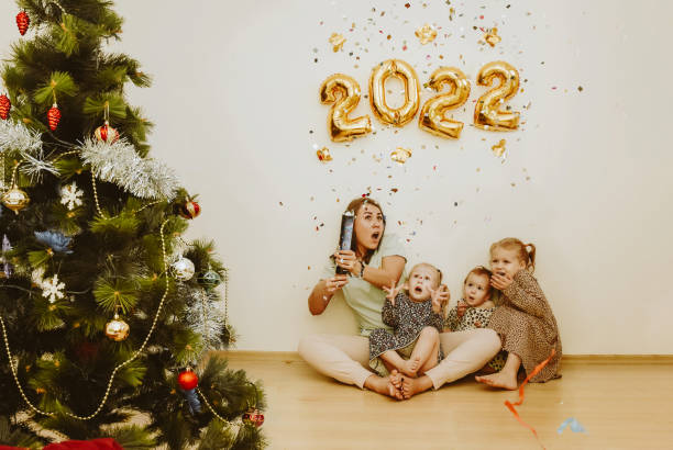 Mom and daughters with real emotions of joy explode a confetti clapper in the New Year 2022 stock photo