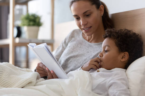 mom and little kid son read book in bed - foster kids imagens e fotografias de stock