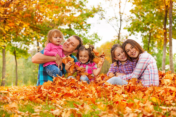 Happy family play with little daughters in the pile of autumn maple...