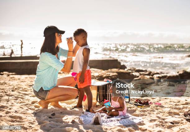 Mom putting suntan lotion on her little children at the beach
