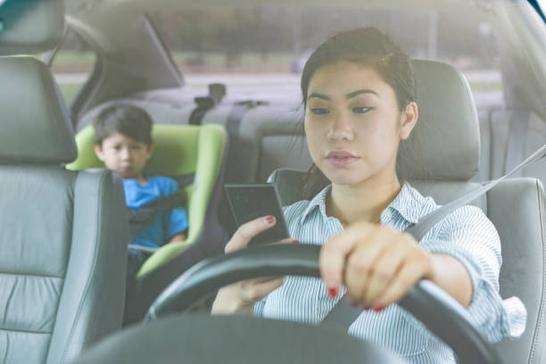 Mom texts while driving with child in the backseat Young mom is driving while distracted while preschool age child is in the backseat. The woman is texting while driving. distracted stock pictures, royalty-free photos & images