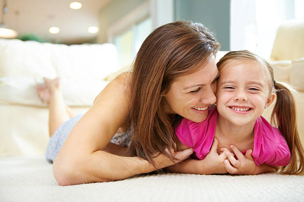 Mommy you're tickling me "Devoted and loving mother snuggles with her cute, gleeful daughter on the lounge carpet" tickling beautiful women pictures stock pictures, royalty-free photos & images