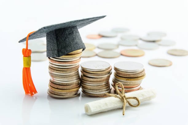 Money cost saving or money reserve for goal and success in school, higher level education concept : US dollar coins / cash, a black graduation cap or hat, a certificate / diploma on white background. stock photo
