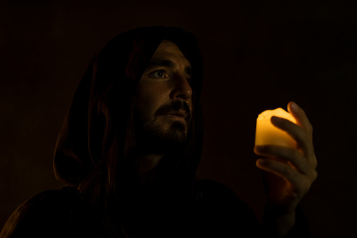 Monk with candle in dark room