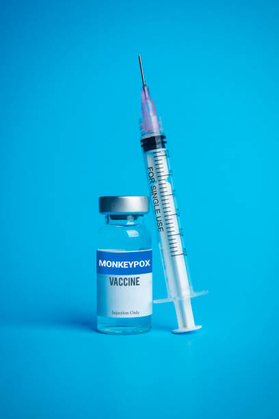 Monkeypox Vaccine With Syringe Leaning A studio shot of a bottle of monkeypox vaccine with a syringe on blue. monkeypox vaccine stock pictures, royalty-free photos & images