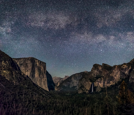 The Yosemite Valley, as seen from Tunnel View, is softly illuminated by the setting moon with the Milky Way above. El Capitan is left, Bridal Veil Falls is to the right and half Dome is in the distant Center.