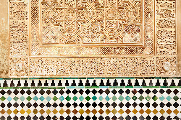 Moorish tiles in the Alhambra, Granada "Tiles and  stonework in the Nasrib Palaces of the Alhambra, in the Mexuar. Carved in the stone are the arms of the Nasrid Dynasty,rulers of Granada from 1232 until 1492. Two different types of highly skilled decorative patterning can be seen in this one section of wall" tessellation stock pictures, royalty-free photos & images