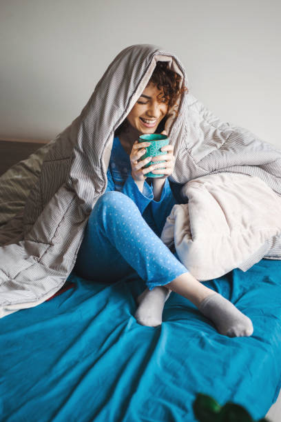 Morning of a curly woman covered by the blanket enjoying a hot drink stock photo
