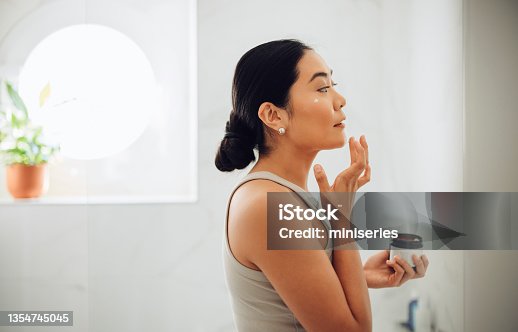 istock Morning Routine: Attractive Asian Woman Applying Face Cream in her Home 1354745045