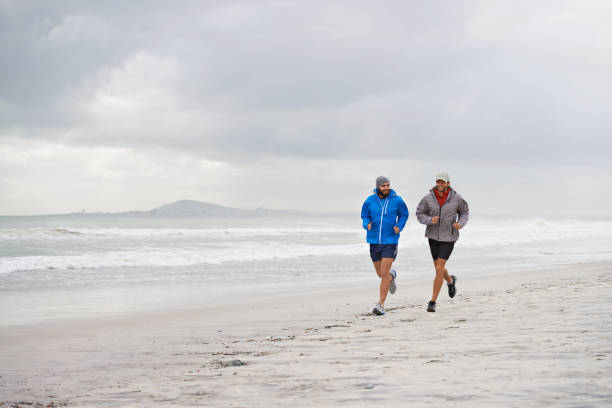 Shot of two men jogging along the beach on an overcast...