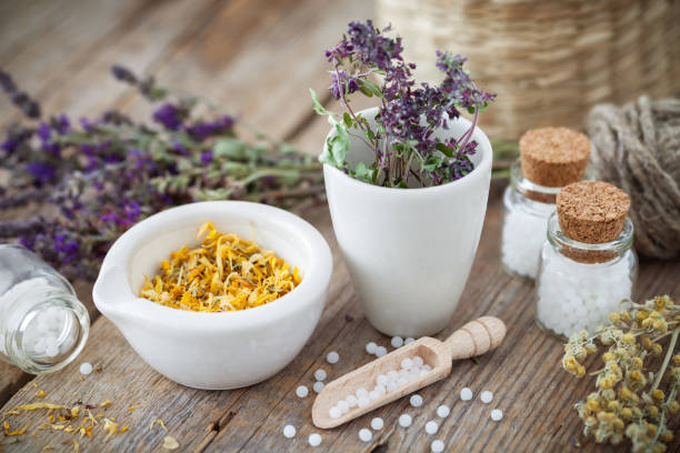 Mortar and bowl of dried healing herbs and bottles of homeopathic globules.  Homeopathy medicine concept. Mortar and bowl of dried healing herbs and bottles of homeopathic globules.  Homeopathy medicine concept. homeopathic medicine stock pictures, royalty-free photos & images