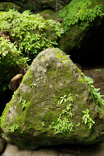 A moss covered rock with a face carved in it, Costa Rica.
