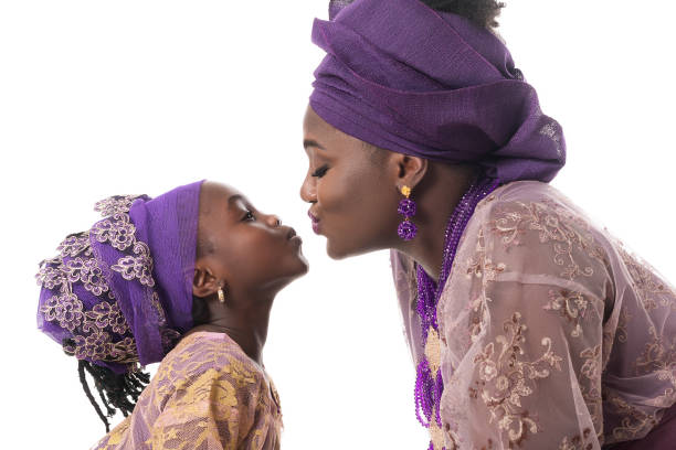 Mother and child girl kissing.African traditional clothing .Isolated Mother and child girl kissing.African traditional purple clothing. Isolated on the white studio background nigeria stock pictures, royalty-free photos & images