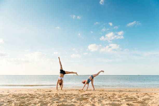 Mother and daughter doing cartwheels at the beach stock photo