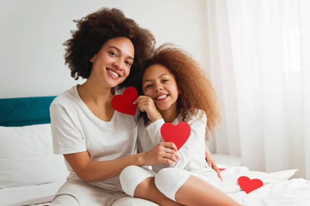 Mother and daughter enjoying on the bed, holding a heart stock photo