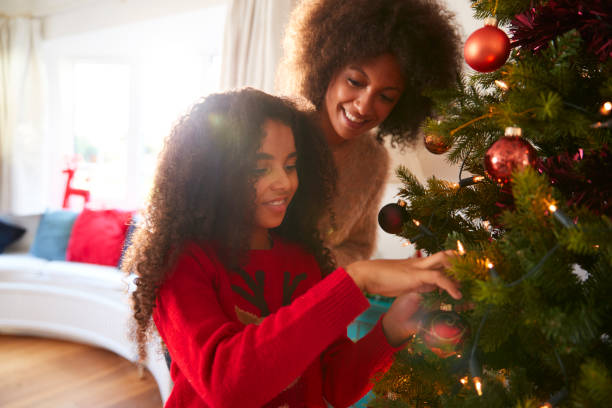 moeder en dochter, opknoping decoraties op de kerstboom thuis - vrouw kerstboom versieren stockfoto's en -beelden