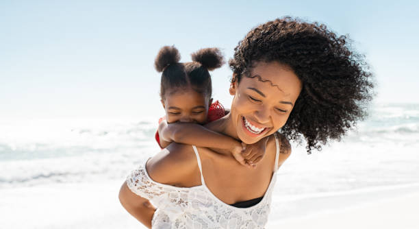 mother and daughter having fun at beach - piggyback funny stockfoto's en -beelden