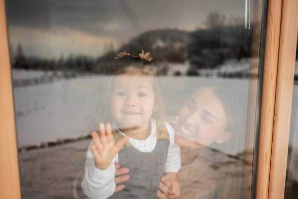 Mother and daughter looking through window stock photo