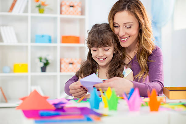 Mother and daughter making origami. Cheerful mother and daughter making origami. Can be also used for education/kindergarten concept. paper art kids stock pictures, royalty-free photos & images